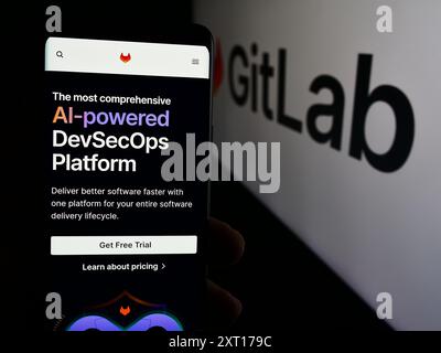 Person holding mobile phone with web page of US open-source software company GitLab Inc. in front of logo. Focus on center of phone display. Stock Photo