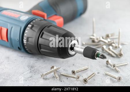 Professional cordless drill screwdriver and screws close-up. Accumulator drill screwdriver with universal holder and screws on concrete surface. Stock Photo