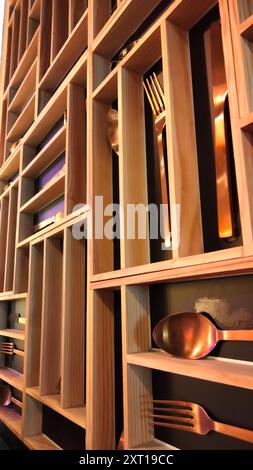 A decorated wall of wooden shelves with silverware on them. The silverware includes forks, spoons, and knives. Intricate layout gives the feeling of a Stock Photo