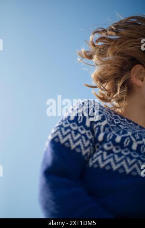 Close-up of a person with curly hair wearing a blue and white patterned sweater against a clear sky. bola02427 Copyright: xConnectxImagesx Stock Photo