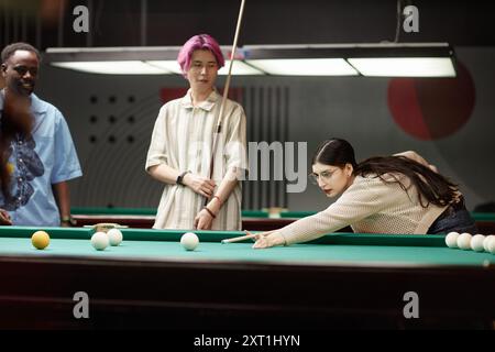 Group of friends enjoying a game of billiards in modern lounge area under ambient indoor lighting creating relaxed vibe Stock Photo