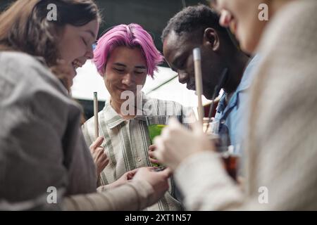 Group of young adults enjoying time together at a modern gathering event while chatting and using gadgets. Multiracial friends forming close connections Stock Photo