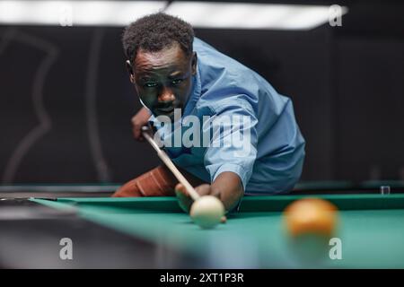 Man focusing on game of billiards, aiming cue ball with intense concentration, ensuring precise shot and form Stock Photo