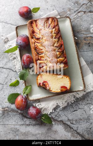 Delicate sponge cake with plums and yogurt close-up in a plate on the table. Vertical top view from above Stock Photo