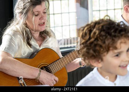 Mature woman playing guitar and singing next to a joyful curly-haired child. panc05868 Copyright: xConnectxImagesx Stock Photo