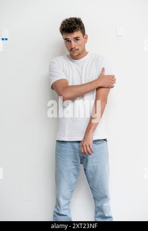 Young man leaning against a white wall with crossed arms and a contemplative expression. panc06074 Copyright: xConnectxImagesx Stock Photo