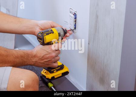 When constructing a house, electrician uses screwdriver to install an outlet on wall Stock Photo