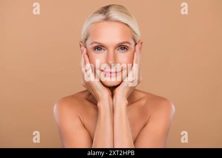 Portrait of adorable charming middle aged lady touch hands cheeks enjoy silky skin after daily morning washing isolated pastel color background Stock Photo