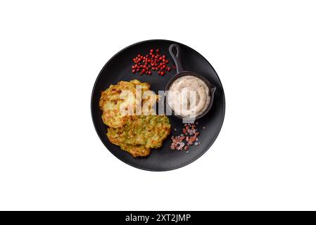 Vegetable zucchini fritters with garlic, salt, spices and herbs with white sauce on a dark concrete background Stock Photo