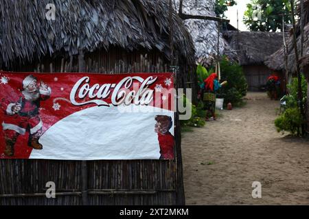 Christmas Coca Cola advert with Santa Claus on wall of a typical bamboo hut, Kuna women in background, Carti Yandup Island, San Blas Islands, Panama Stock Photo