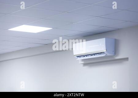A wall-mounted air conditioner in a room with a tiled ceiling, showcasing modern climate control technology. Copy space. Stock Photo