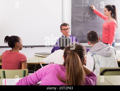 Cute student girl solves task near blackboard in classroom mathematics Stock Photo