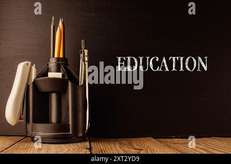 A pencil holder with pencils and a pen sits on a wooden table. The word education is written on the table Stock Photo