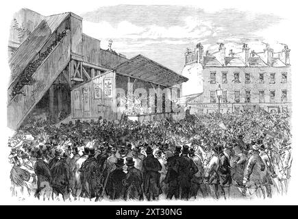 Nomination at the Southwark Election, 1870. Crowds in south London. 'This proceeding had, on former occasions, taken place in the old Townhall, in High-street, Borough; but that building has lately been demolished by the Corporation for street improvements; and the hustings were, therefore, erected on a piece of vacant ground near the Borough-road station of the London, Chatham, and Dover Railway. The High Bailiff, Mr. Gresham, opened the business at eleven o'clock, when a dense crowd of people surrounded the hustings, upon which stood the candidates and their friends, exposed to the keen nort Stock Photo