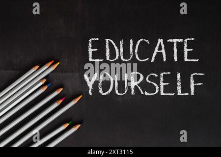 A chalkboard with the words educate yourself written on it. The chalkboard is surrounded by a row of pencils, which are of different colors Stock Photo
