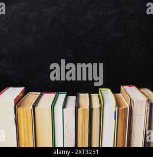 A row of books on a black chalkboard. The books are of different sizes and colors. The books are arranged in a neat row, with the largest book on the Stock Photo