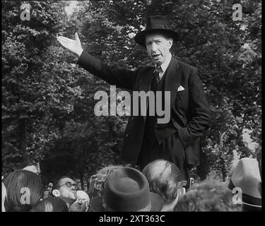 A Close up of a British Man in Dark Suit and Hat Declaiming Before a Crowd from a Raised Lectern at Speaker's Corner, Hyde Park, With Right Hand Gesturing and Left Hand in His Trouser Pocket, 1938. From &quot;Time To Remember -  Wind up Week&quot;, 1938 (Reel 2); documentary film about 1938 - people become aware of the growing threat of war. Stock Photo