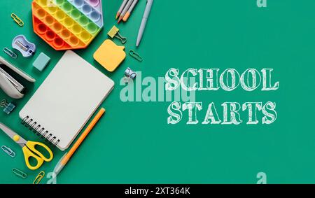 A green background with school supplies and a notebook with the words school starts written on it. The supplies include a pen, scissors, and a ruler Stock Photo