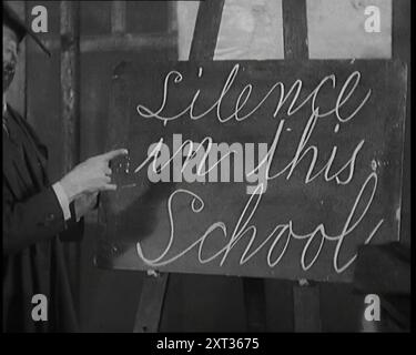 The Entertainer Will Hay Writing on a Blackboard, the Board Reads: 'Silence in this School', 1920s. London stage show. 'The headmaster of music hall himself, Will Hay, as always hard-pressed to outwit his bright but unruly pupils'. From "Time To Remember - On Stage in the Twenties", 1927 (Reel 3); a look behind the scenes of the theatre during the 1920's. Stock Photo