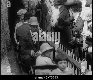 King George V and Queen Mary of the United Kingdom Sit in a Model Train As It Passes Through a Tunnel. A Crowd of People Watch from Behind a Fence, 1924. From &quot;Time To Remember - A Trip To Europe&quot;, 1924 (Reel 3); a look at political and social life in Europe and beyond during 1924. Stock Photo