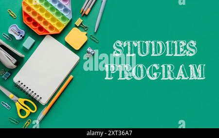 A green background with a notebook, pens, and scissors. The word studies is written in white letters on the right side of the image Stock Photo