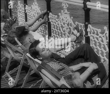 A Woman Sleeping in a Deckchair by Railings on the Promenade at Brighton With a Man and Two Other Women to Her Left, 1939. From &quot;Time To Remember -  The Reluctant Warriors&quot;, 1939 (Reel 1); documentary about events of 1939 - preparations for war and then hostilities break out. Stock Photo