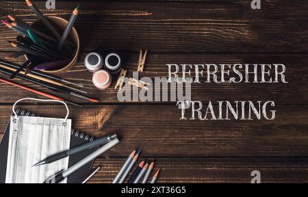 A wooden table with a bowl of colored pencils and a bottle of paint. The words Refresher Training are written on the table Stock Photo