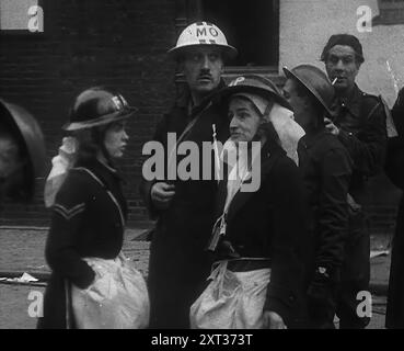 Civil Defence Corps Members, 1940. Britain during the Second World War: the Blitz. The man in the centre is a Medical Officer. 'Any night, any time, summer 1940. Fire and flame, death and destruction...Any morning-after in London - or is it Coventry, Bristol, Portsmouth? Liverpool, Belfast, Birmingham? Plymouth or Glasgow?...Good morning, toilers of the night, time you were in bed - you've earned it'. From &quot;Time To Remember -  Standing Alone&quot;, 1940 (Reel 4); documentary film about events of later months of 1940. Stock Photo