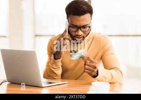 African man talking on phone holding credit card Stock Photo