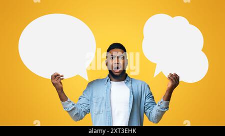 Confused black guy holding two speech bubbles on yellow background Stock Photo