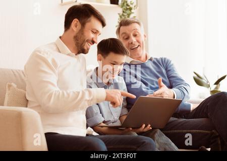 Boy Using Laptop Sitting Between Father And Grandfather On Couch Stock Photo
