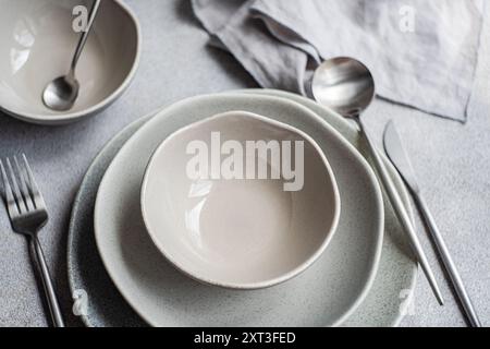 An elegantly arranged minimalist table, with gray textured tableware and matching stainless steel cutlery, all neatly placed on a matte tablecloth The Stock Photo