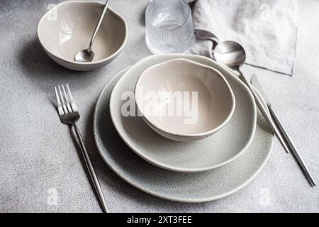 A simple and elegant table setting features a stack of ceramic plates and bowls in neutral tones, complemented by sleek metal forks and spoons The sof Stock Photo