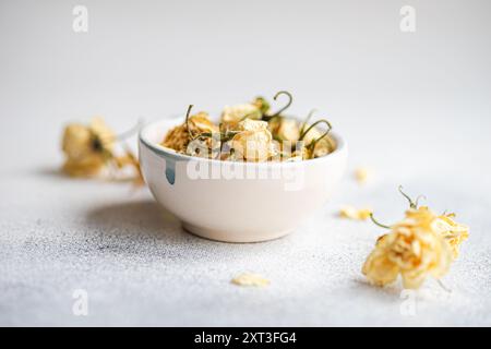 A ceramic bowl filled with delicate dried roses rests against a soft, textured white background, offering a simplistic yet elegant decorative theme Stock Photo
