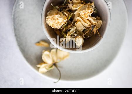 A close-up shot of withered roses in muted tones, placed in a simplistic gray ceramic bowl, conveying a theme of decay and nostalgia Stock Photo
