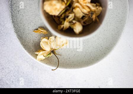A delicate, dried rose rests inside a speckled ceramic bowl, set against a white linen background, evoking a serene and minimalist aesthetic Stock Photo