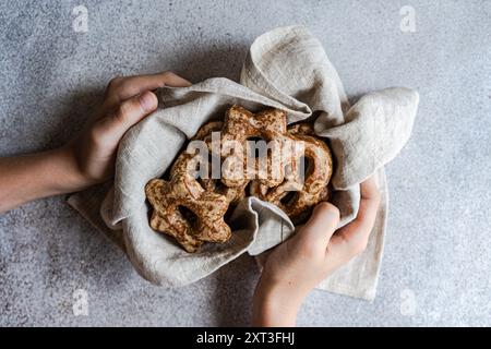 Top view of cropped unrecognizable hands holding a cloth filled with homemade gingerbread cookies shaped like stars, presented on a textured grey surf Stock Photo