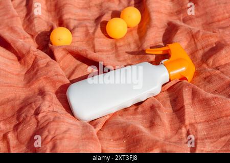 A sunscreen spray bottle lies on a vibrant orange cloth, surrounded by small orange balls This scene emphasizes summer essentials, combining color and Stock Photo