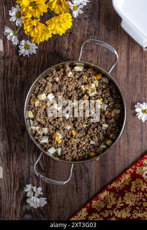 Top view of a freshly prepared homemade meat pie filling in a stainless steel pan, featuring ground meat, potatoes, and boiled eggs on a rustic wooden Stock Photo