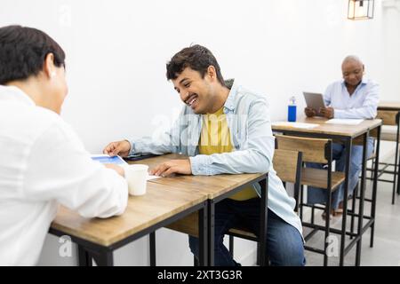 A cheerful scene of adult students interacting in an English academy, sharing thoughts and learning collaboratively in a bright classroom setting Stock Photo