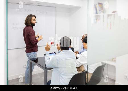 An engaging instructor interacts with adult students in a modern English language academy, illustrating concepts on a whiteboard as attentive particip Stock Photo