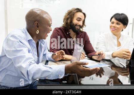 A team of three diverse students engaged in a lively discussion in a bright classroom, displaying effective collaboration and teamwork Stock Photo