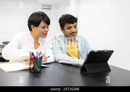 Two adult students participate in a collaborative learning session using a digital tablet within a well-lit classroom, fostering a dynamic educational Stock Photo