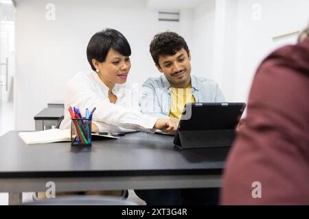 Two adult students, a man and a woman, engaged in a collaborative learning session at an English language academy They are focused on a digital tablet Stock Photo