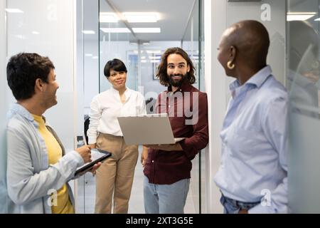 Four colleagues discuss a project using a laptop The team, which seems committed and cooperative, is in a modern language academy Stock Photo