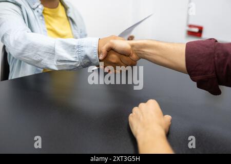 A professional handshake between two individuals at a table, symbolizing teamwork and collaboration in an English academy context Stock Photo