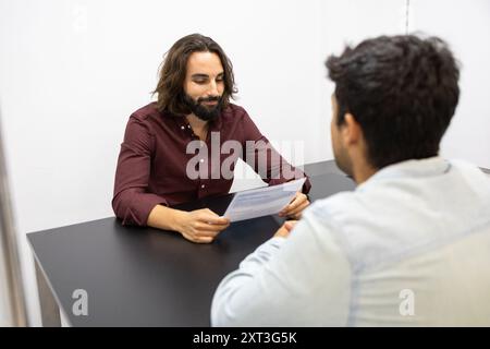 Two adult male students engage in a focused discussion over paperwork at a simple office setup, reflecting effective teamwork and communication in an Stock Photo