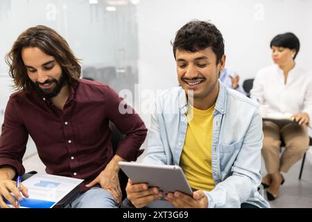 Two male colleagues engage in a collaborative discussion, reviewing content on a digital tablet during an educational workshop in a modern office sett Stock Photo