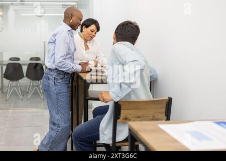 Three people collaborate around a table in an English academy, discussing educational materials The scene depicts teamwork and learning Stock Photo
