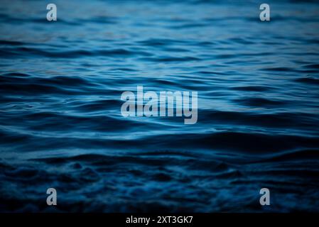 This image captures the peaceful waves of the sea under a dim light, highlighting the subtle texture and gentle movement of the water The serene blue Stock Photo